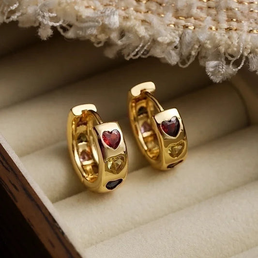 Gold hoop earrings with red gemstones on a beige cushion